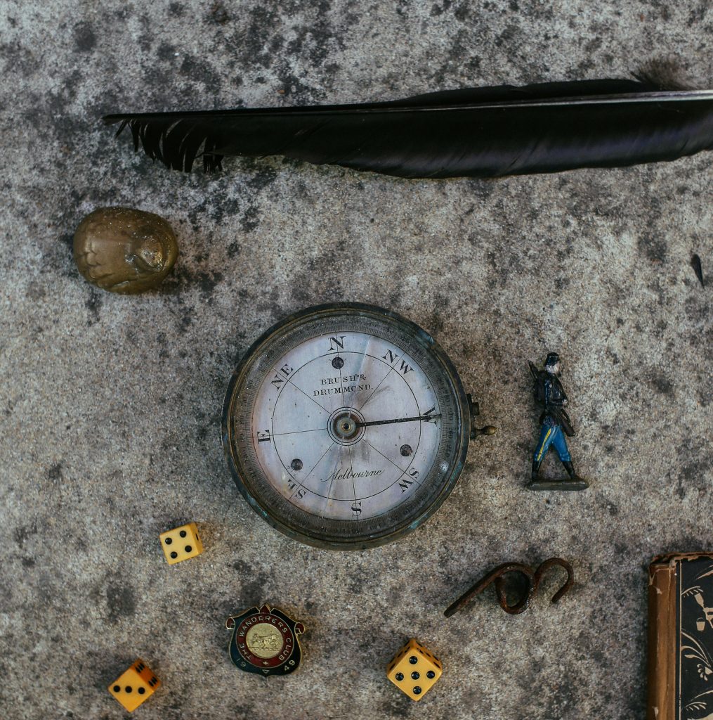 pexels-photo-5863561-5863561 Top view of vintage items including compass, feather, and dice on stone surface.