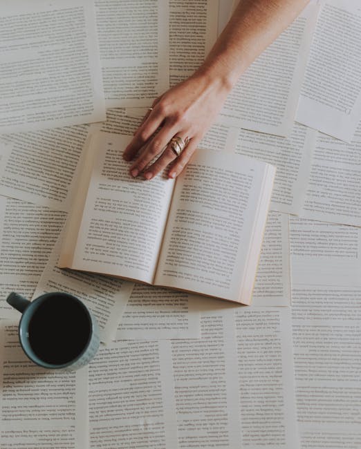 A hand reaching over an open book surrounded by pages with a coffee cup nearby, creating a cozy reading scene.