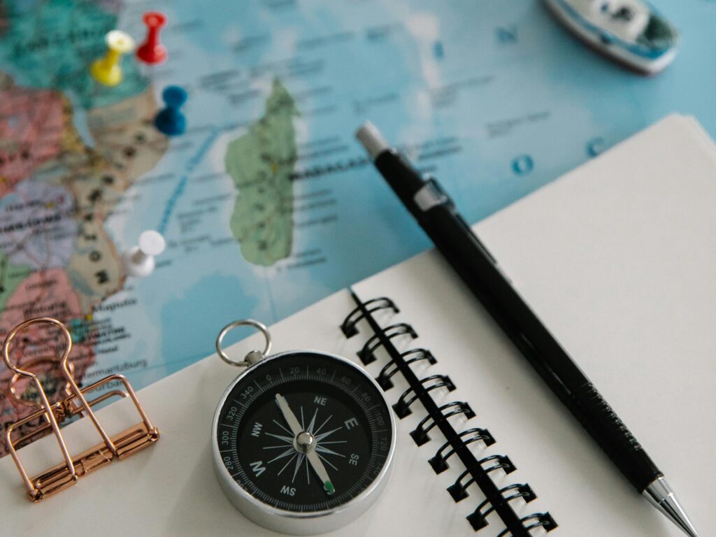 pexels-photo-8828668-8828668 Flat lay of travel essentials including a navigational compass, pencil, notepad, and map for trip planning.